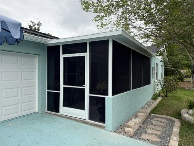 Screen enclosure with white aluminum frame, black screening, and hinged door on turquoise home