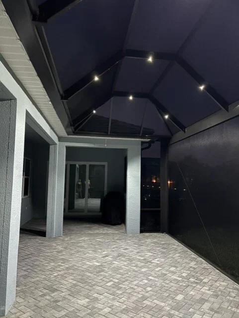 Black peaked roof patio enclosure with white columns, recessed lighting, and herringbone pavers