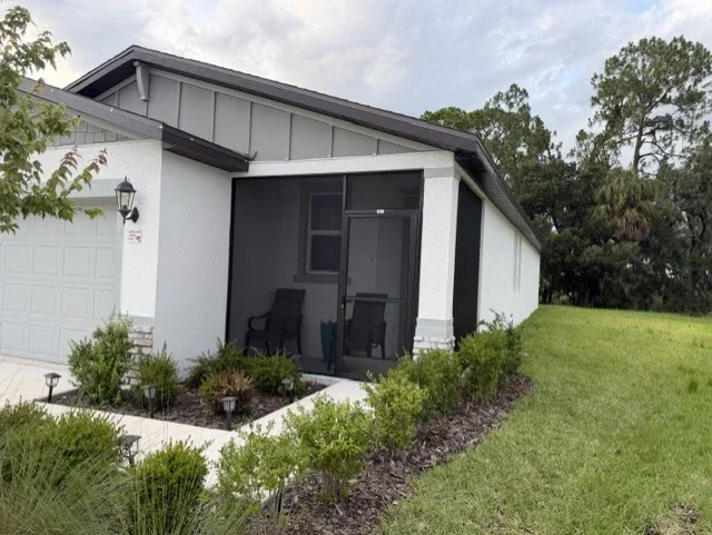 Black-framed screen enclosure with mesh screening attached to white house with landscaping
