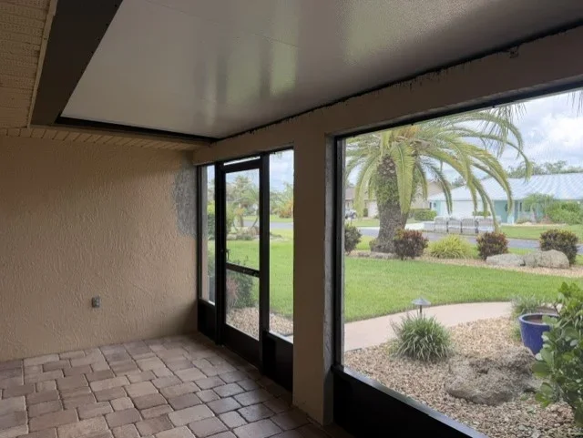 Screen enclosure with black aluminum frame, glass doors, and clay brick paver flooring overlooking landscaped yard